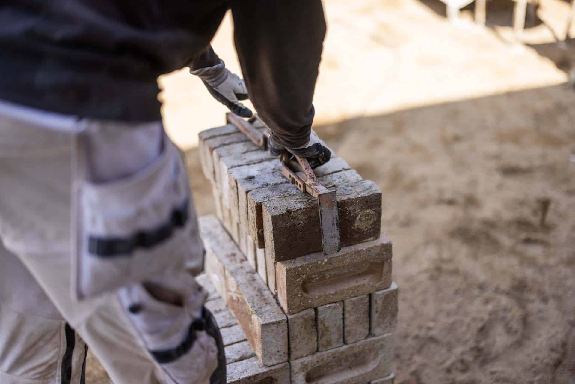 Mursten lægges i mørtel, mens et vaterpas bruges til at kontrollere murens præcision.