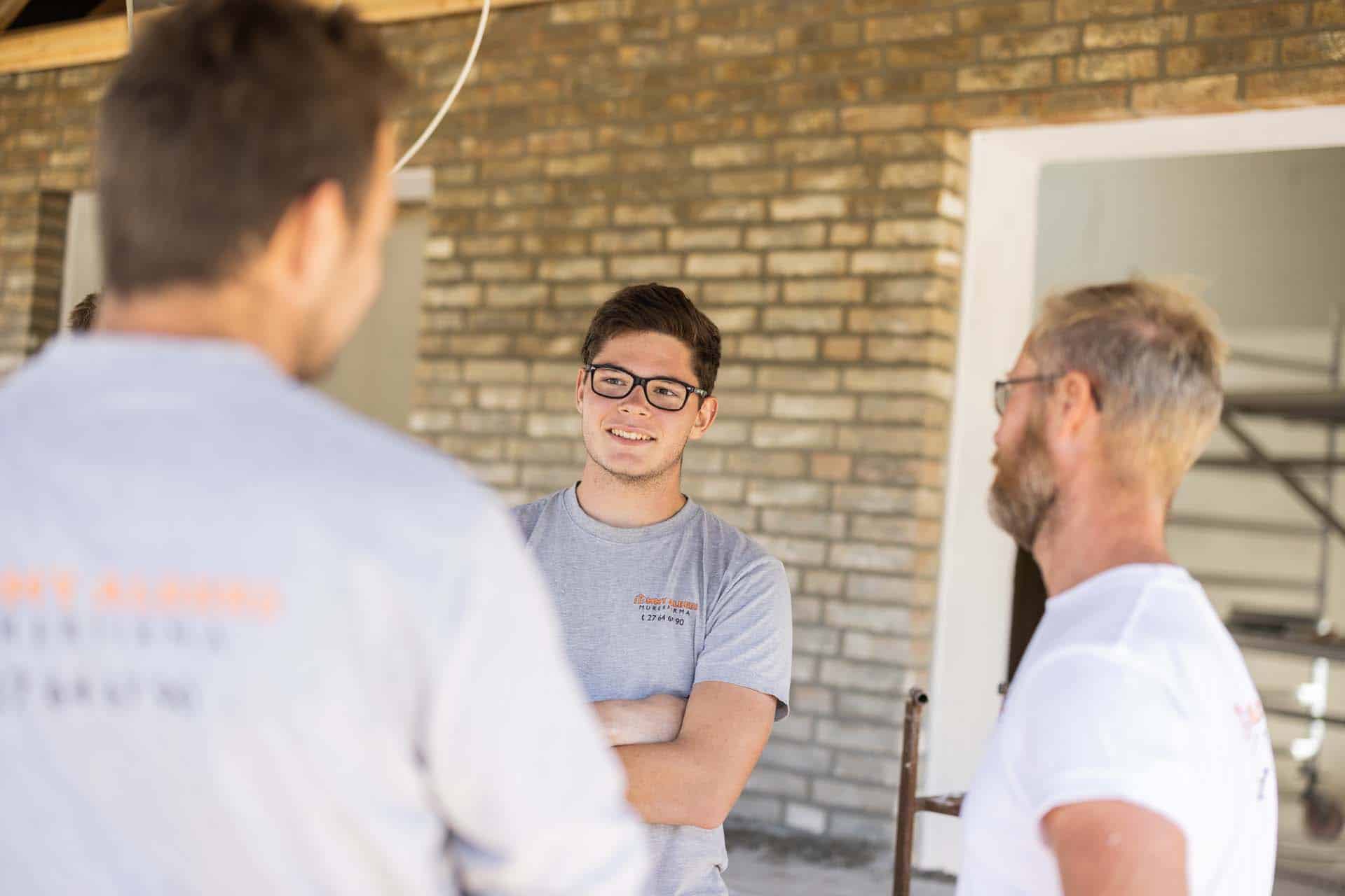 Tre medarbejdere i samtale foran et murstenshus.