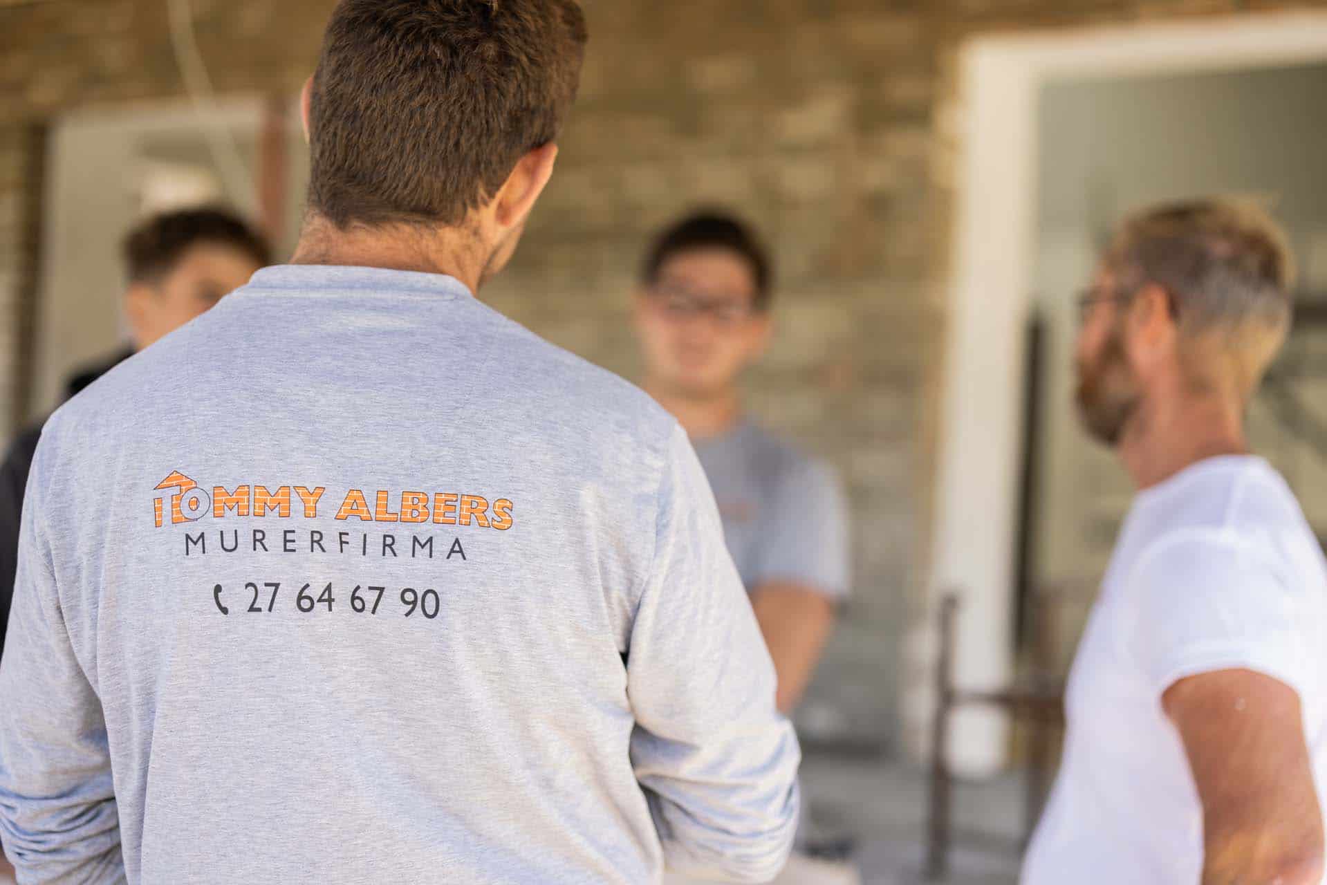 Fire medarbejdere, hvor firmatrøjen hos den ene fremhæves i skarp fokus, mens resten af motivet er sløret.